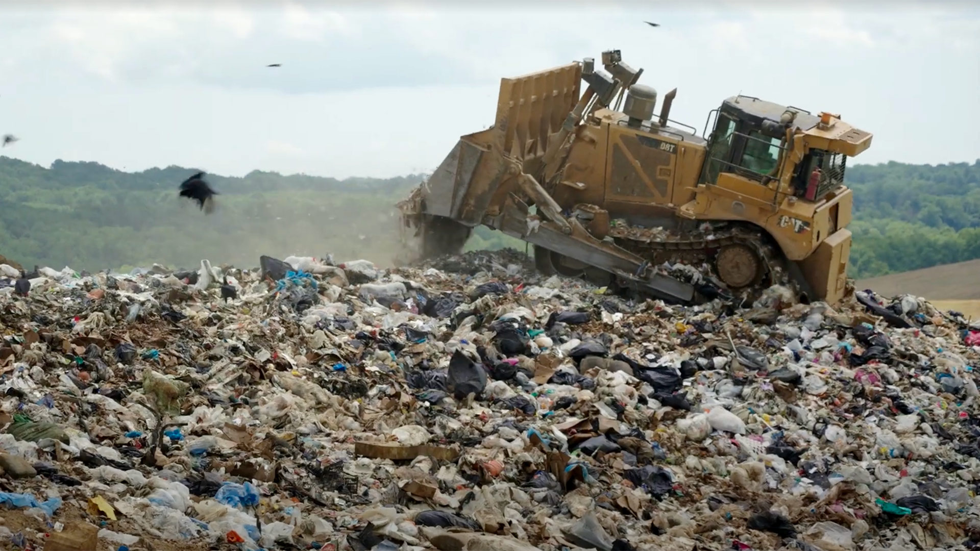 A tractor riding over a large mound of trash