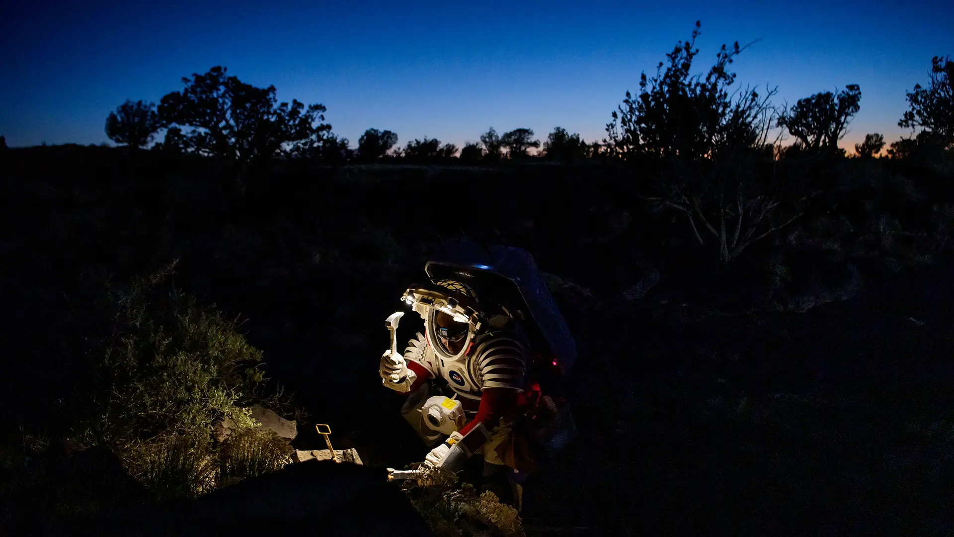 Astronaut Andre Douglas breaks off a small rock sample during a nighttime simulated moonwalk in Arizona.